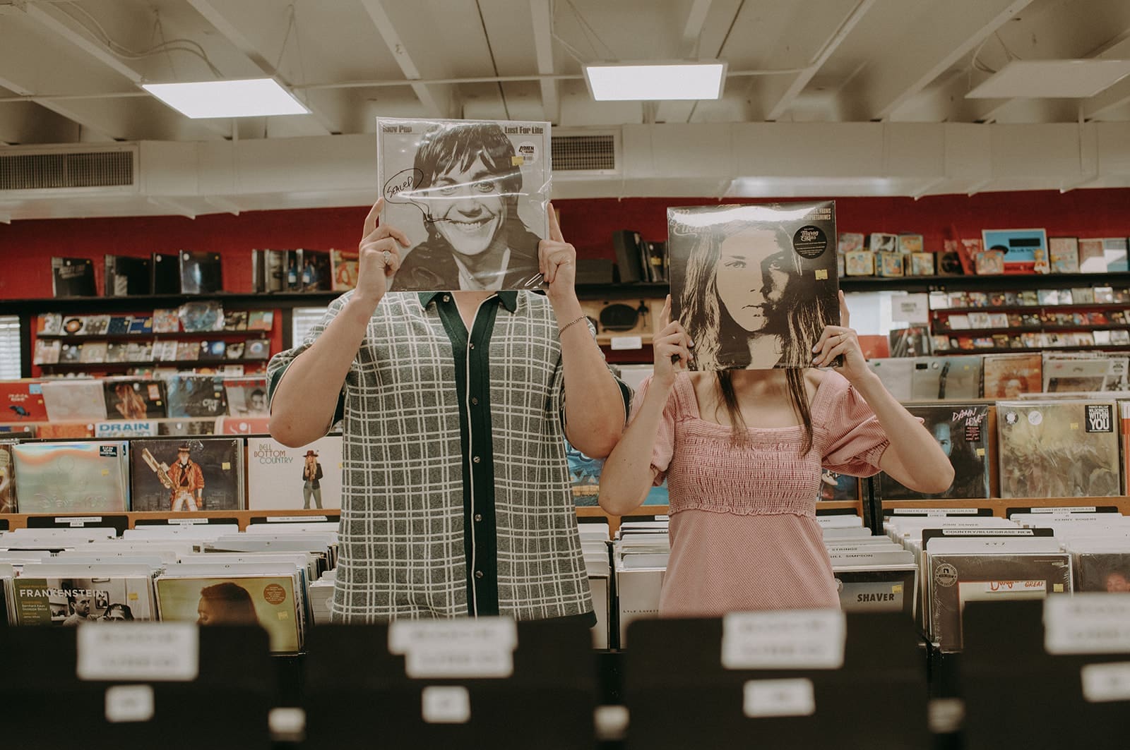 couple with vinyl records in front of their faces at a record store in plaza midwood, charlotte north carolina