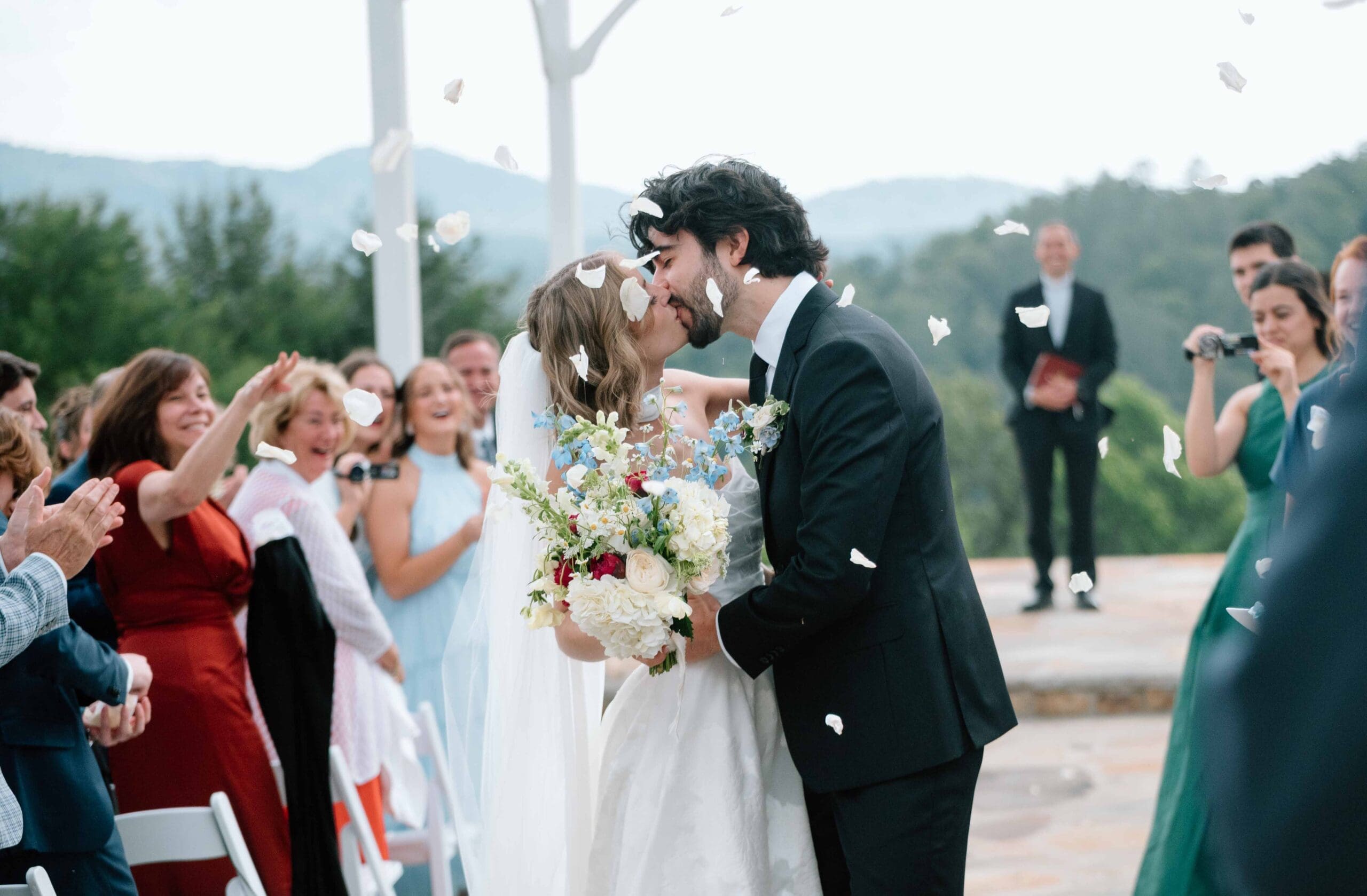 bride and groom walking down the aisle on their ceremony exit while guests are tossing dry flower petals at henderson acres, weaverville, north carolina